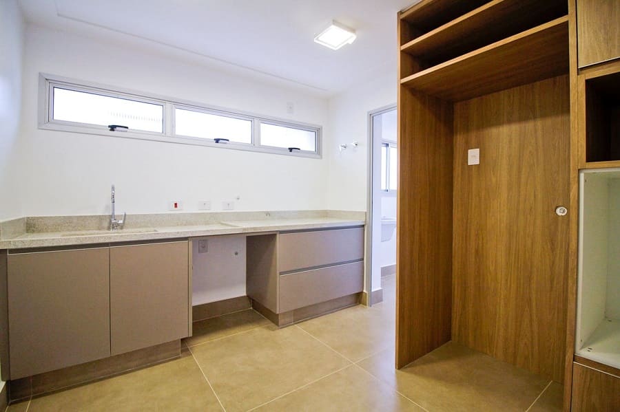 Foto do antes da reforma mostrando o estado original da cozinha, com marcenaria básica, piso claro e nichos vazios para eletrodomésticos, no apartamento na Vila Olímpia, São Paulo.
