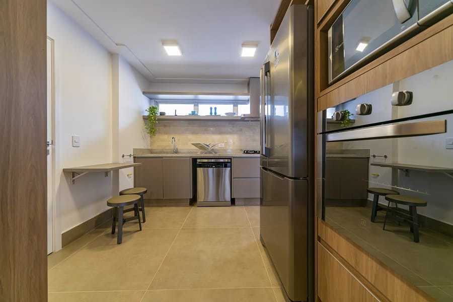 Cozinha moderna com piso claro, mesa retrátil de apoio e eletrodomésticos em inox, compondo o projeto de interiores de um apartamento na Vila Olímpia, São Paulo.