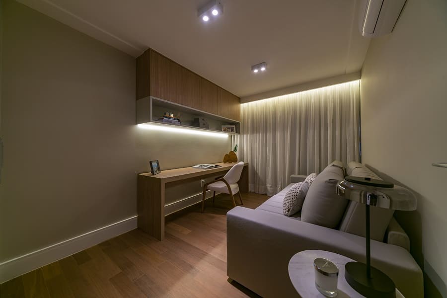 Ambiente multifuncional projetado como home office e quarto de hóspedes, com bancada de madeira, iluminação indireta em fita LED e sofá-cama em apartamento na Vila Olímpia.