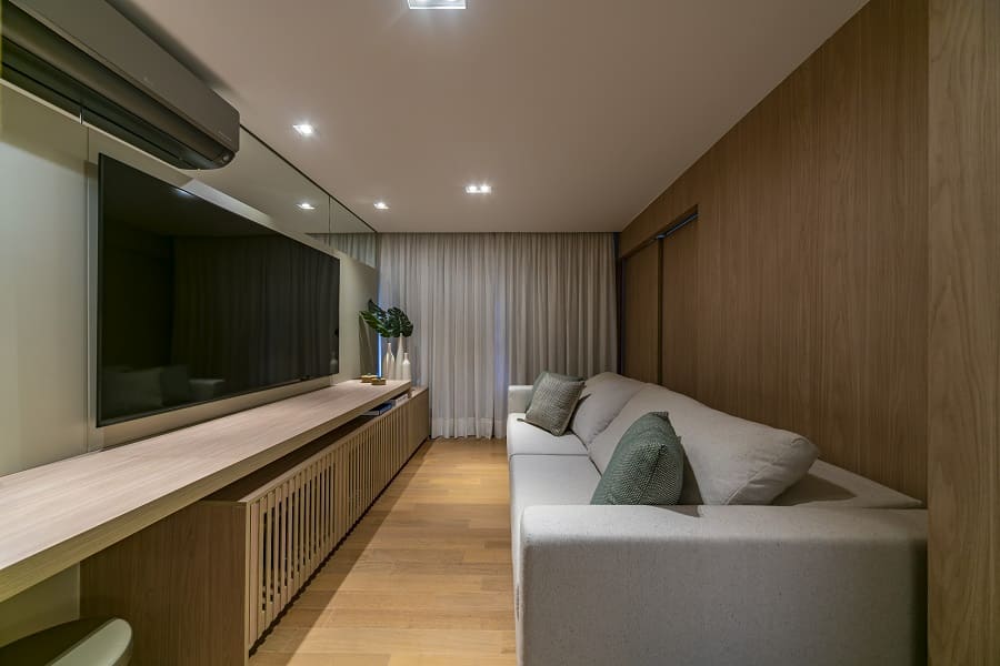 Visão da sala de TV com a porta de correr de madeira fechada, garantindo privacidade para o uso como quarto de hóspedes no apartamento na Vila Olímpia, São Paulo.