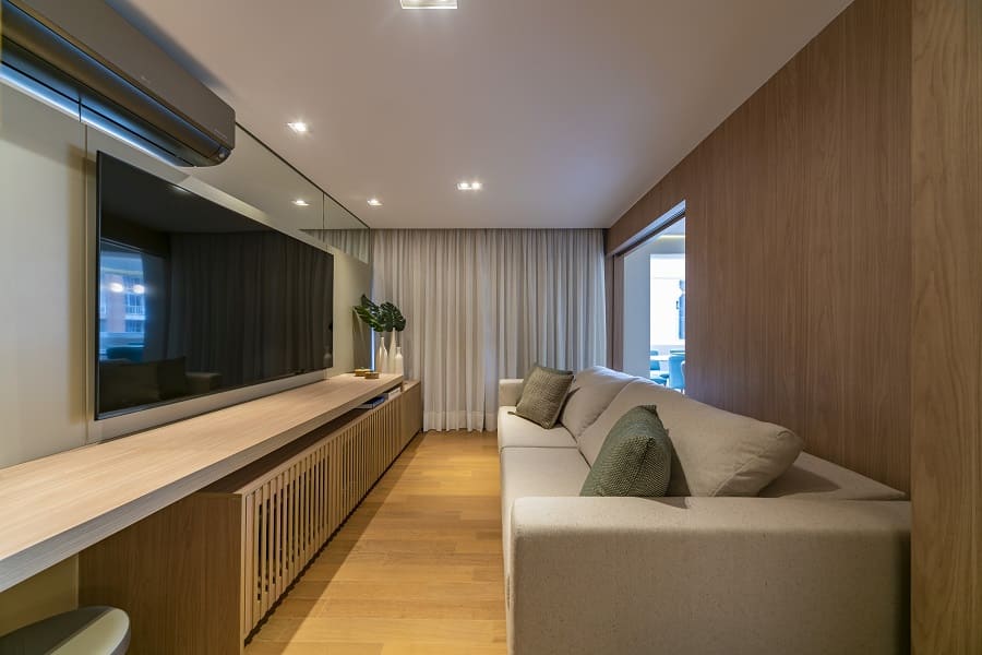 Visão da sala de TV com a porta de correr de madeira aberta, mostrando a integração fluida com o restante da área social no projeto do apartamento na Vila Olímpia, São Paulo.