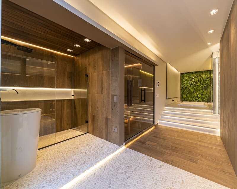 Vista integrada do spa com sauna de vidro ao fundo e porta de acesso para a área gourmet em residência de Alphaville.