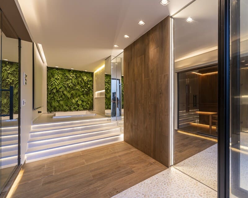 Detalhe do piso em porcelanato amadeirado com faixa de seixos brancos ao redor do spa e parede com jardim suspenso.