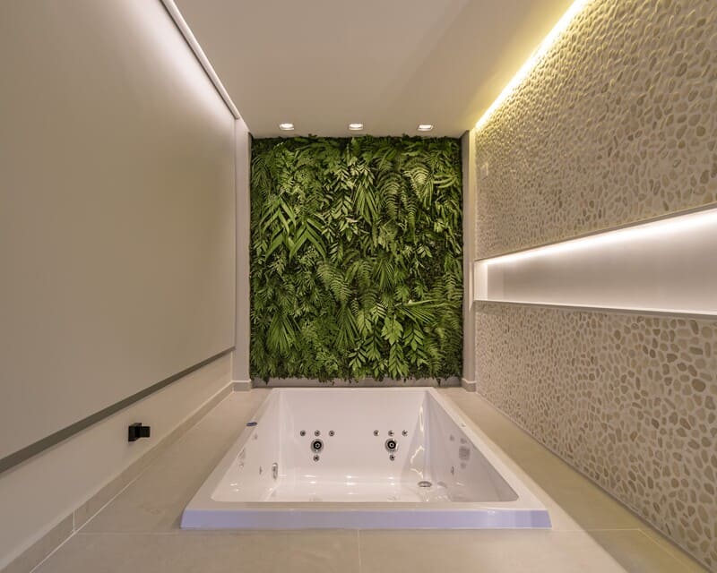 Nicho iluminado na parede do spa com luz indireta quente, velas decorativas no degrau e cesto de toalhas.