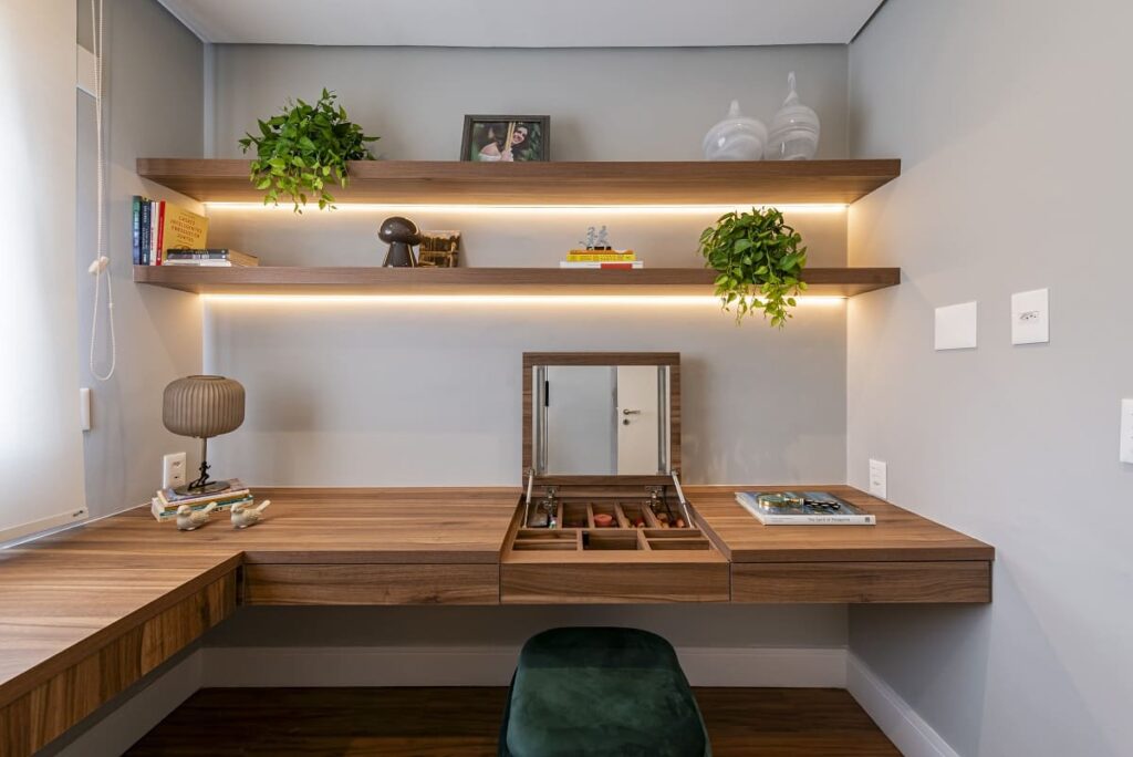 Visão frontal da bancada multifuncional de madeira no home office. No centro, o tampo está levantado funcionando como uma penteadeira com espelho. Projeto de apartamento no Jardim Caravelas, São Paulo, por Thais Guarizo.