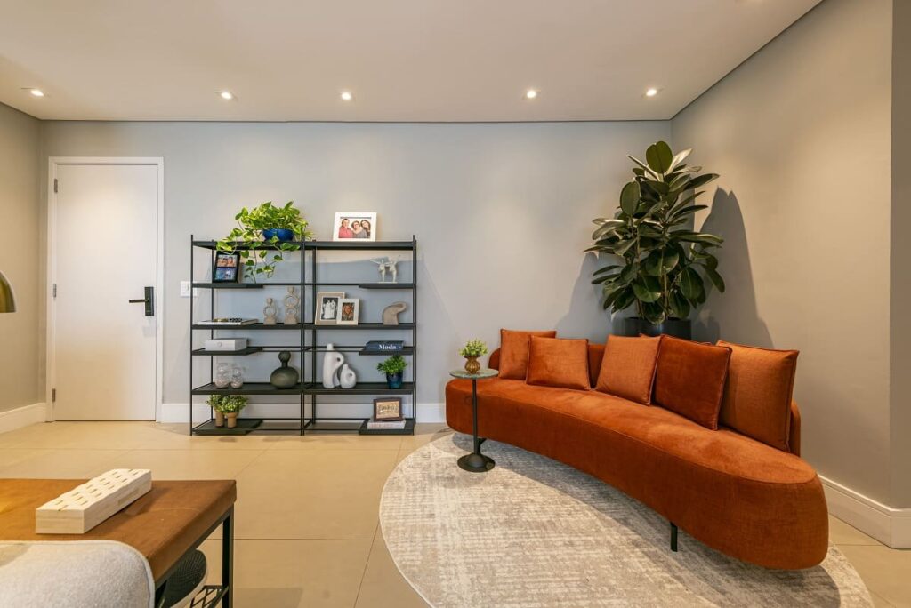 Hall de entrada moderno com sofá curvo na cor terracota, tapete redondo e uma estante preta de estilo industrial. Design de interiores no Jardim Caravelas, São Paulo, por Thais Guarizo.
