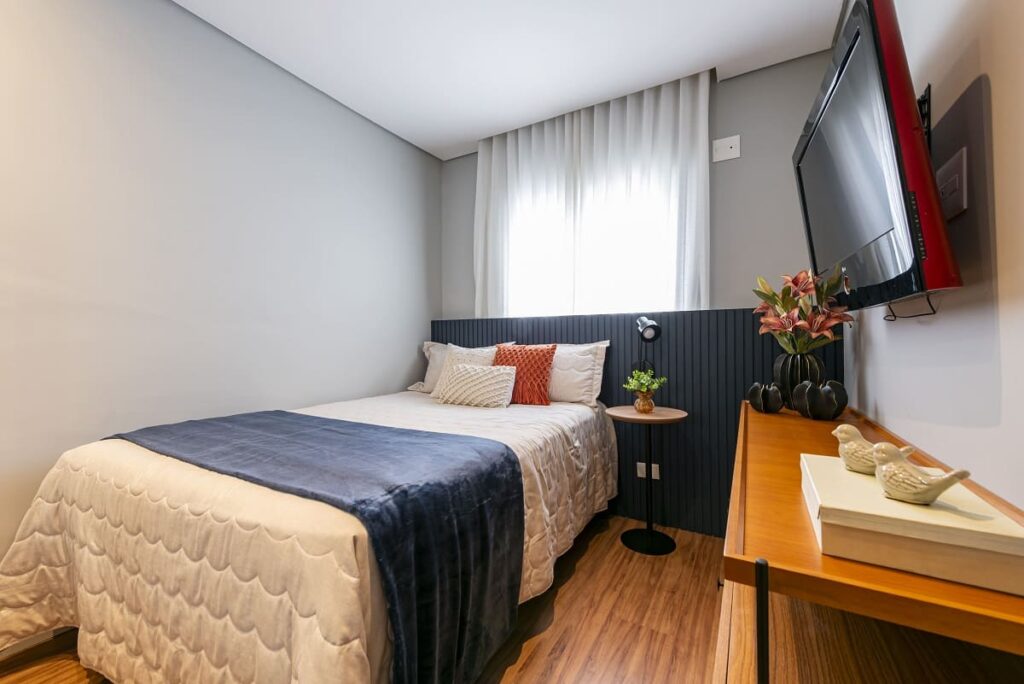 Quarto de visitas acolhedor com cama de solteiro, destacando a cabeceira ripada e laqueada em azul marinho e enxoval em tons neutros. Projeto arquitetônico assinado pela arquiteta Thais Guarizo em São Paulo.
