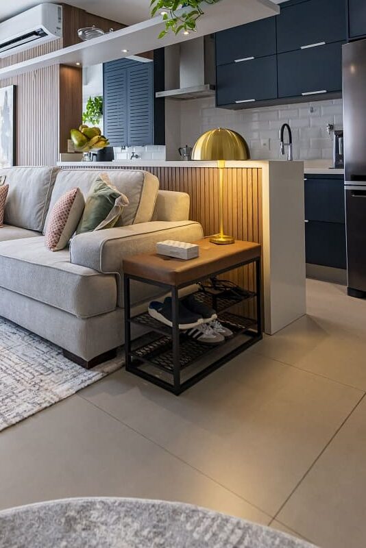 Sala de estar confortável com sofá claro, totalmente integrada à cozinha moderna com marcenaria em azul petróleo e bancada branca. Arquitetura de interiores em São Paulo, arquiteta Thais Guarizo.